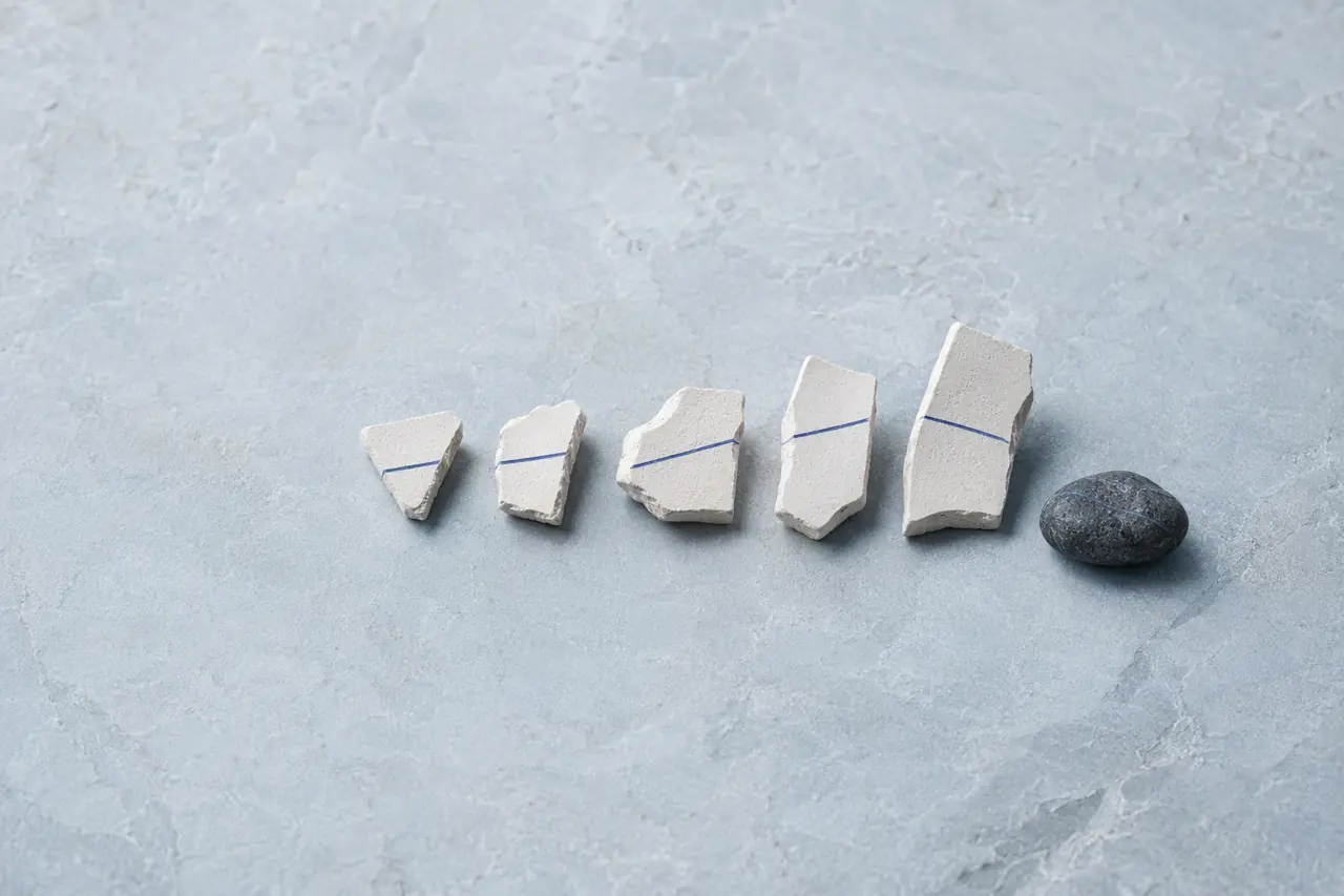Five pale ceramic fragments marked by a cobalt line beside one dark stone, arranged like a run timeline